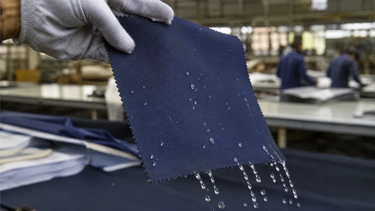 Water droplets beading on a dark navy uniform twill swatch tilted on a mill inspection bench