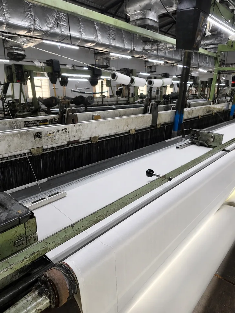 Wide view of the weaving hall with rolls of woven fabric on the looms at the Bhilwara mill