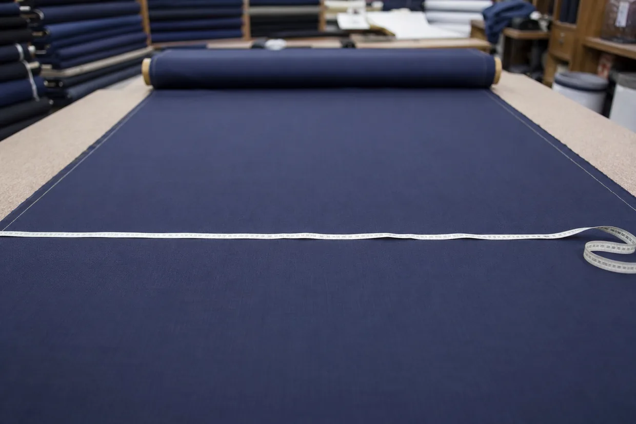 Fabric width being measured with a tape across an unrolled navy suiting roll on a cutting table