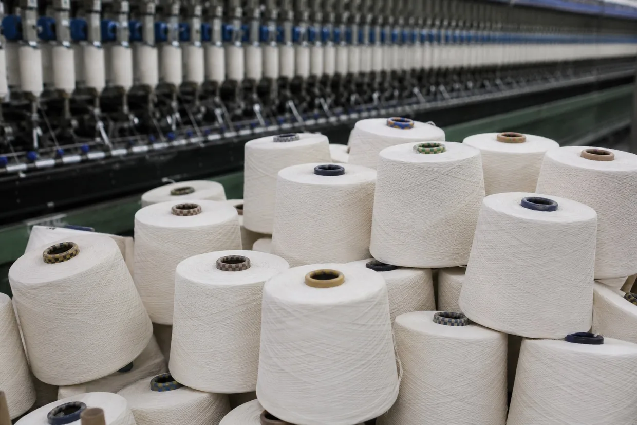 Stacked cones of raw white yarn in front of a spinning frame